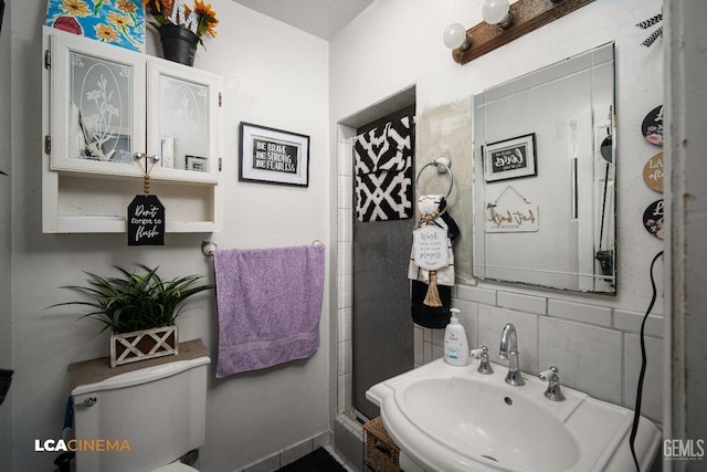 bathroom with decorative backsplash, a shower stall, toilet, and a sink