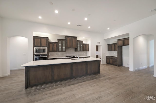 4414 Coal Rock Ct, Bakersfield, CA 93313 - kitchen with arched walkways, appliances with stainless steel finishes, decorative backsplash, a spacious island, and dark brown cabinetry