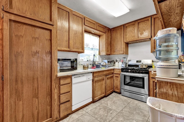 1504 Stockton Ave, Bakersfield, CA 93308 - kitchen featuring white dishwasher, stainless steel gas range, light countertops, brown cabinetry, and light tile patterned floors