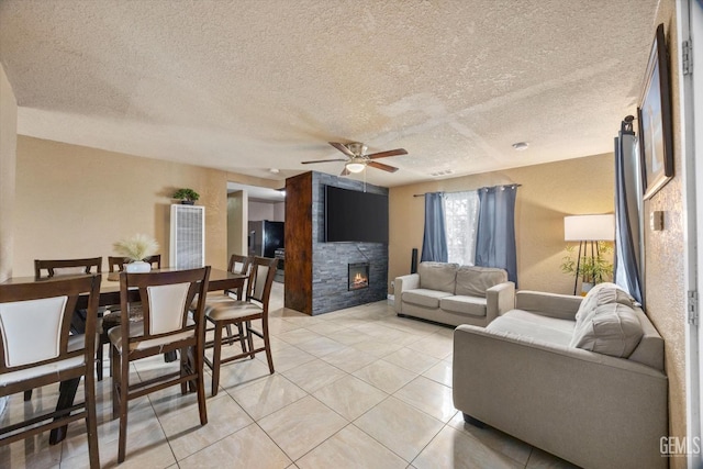 living room featuring a textured ceiling, a fireplace, a ceiling fan, and light tile patterned flooring