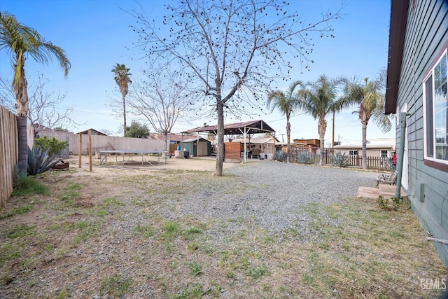 view of yard featuring a trampoline, a fenced backyard, an outdoor structure, and a storage unit