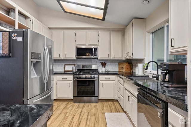 kitchen featuring lofted ceiling, a sink, appliances with stainless steel finishes, light wood finished floors, and tasteful backsplash