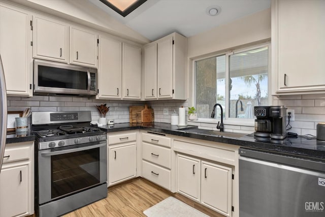 kitchen featuring stainless steel appliances, decorative backsplash, white cabinets, a sink, and light wood-type flooring