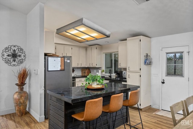 kitchen with light wood finished floors, tasteful backsplash, dark countertops, and freestanding refrigerator