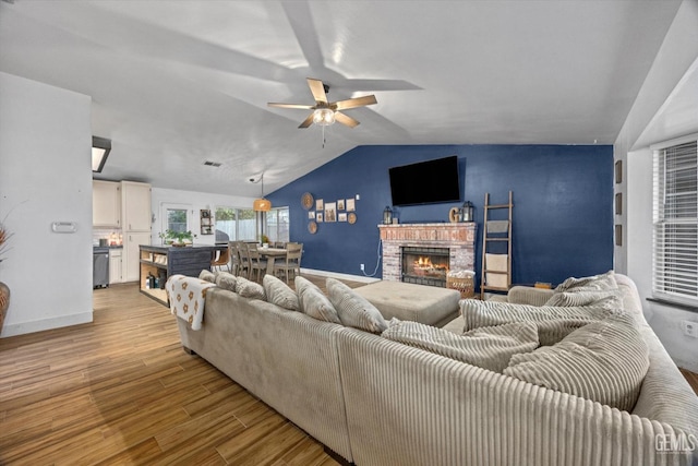 living area with light wood finished floors, lofted ceiling, a brick fireplace, ceiling fan, and baseboards