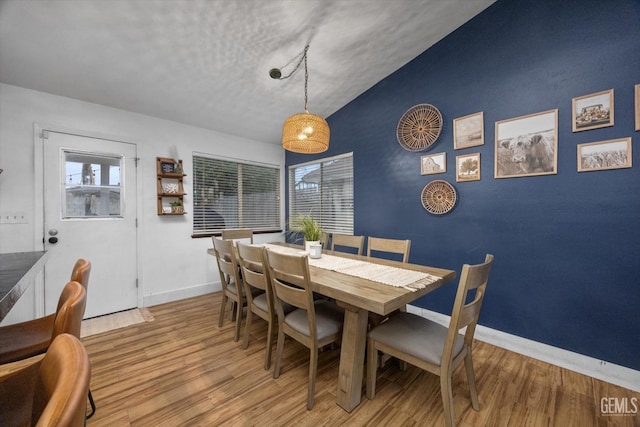 dining space with an accent wall, baseboards, vaulted ceiling, and wood finished floors