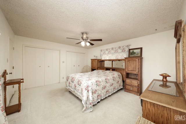 bedroom featuring a textured ceiling, a ceiling fan, multiple closets, and light colored carpet