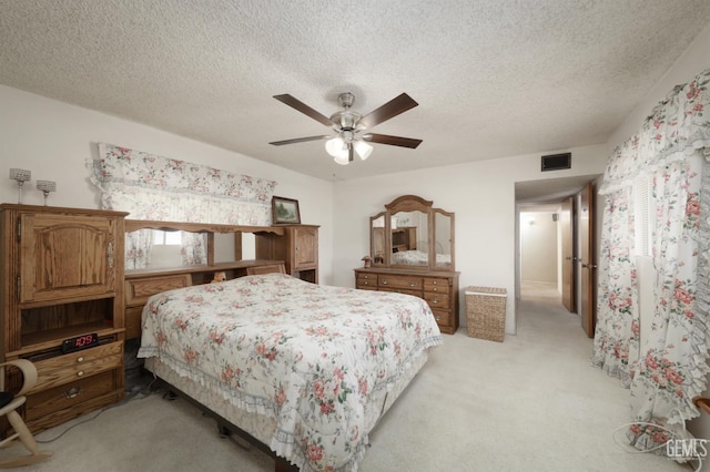 bedroom with a textured ceiling, a ceiling fan, visible vents, and light colored carpet