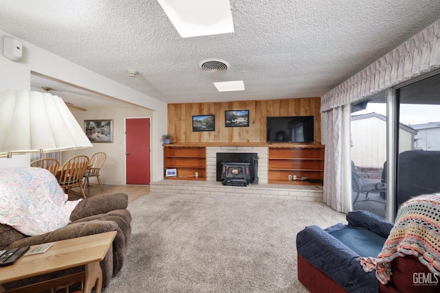 carpeted living room featuring a textured ceiling, a wood stove, visible vents, and wooden walls