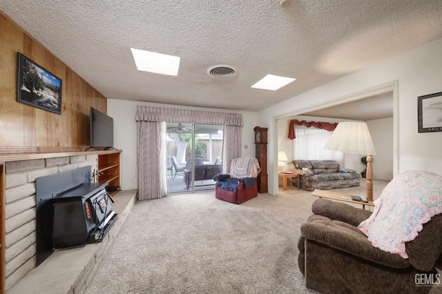 carpeted living room featuring plenty of natural light, wooden walls, visible vents, and a textured ceiling