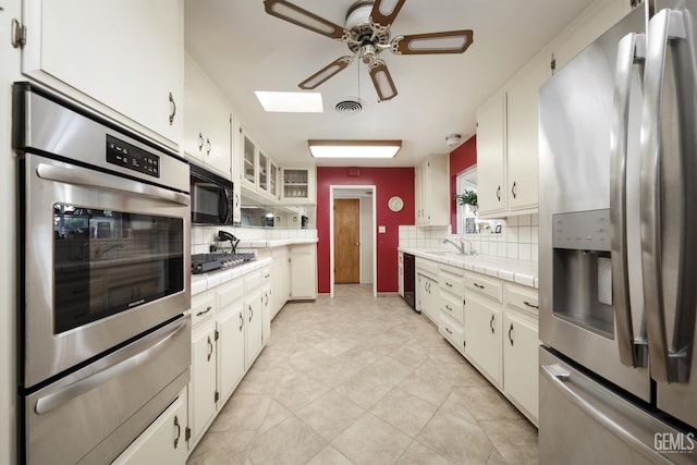 kitchen featuring tile countertops, visible vents, a warming drawer, black appliances, and tasteful backsplash