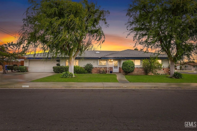 ranch-style house with brick siding, concrete driveway, a tiled roof, stucco siding, and a front yard