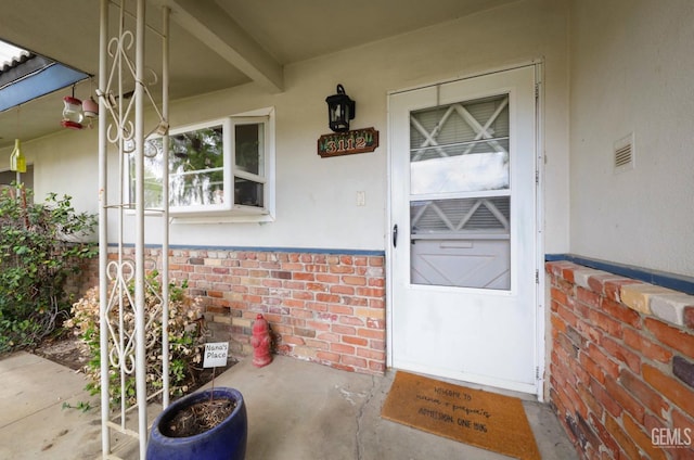 property entrance featuring crawl space, stucco siding, and brick siding