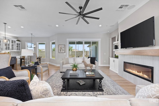 living room featuring ceiling fan with notable chandelier, light hardwood / wood-style floors, and built in features