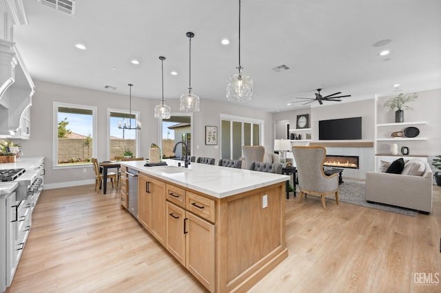 kitchen featuring a center island with sink, sink, ceiling fan, built in features, and light brown cabinetry