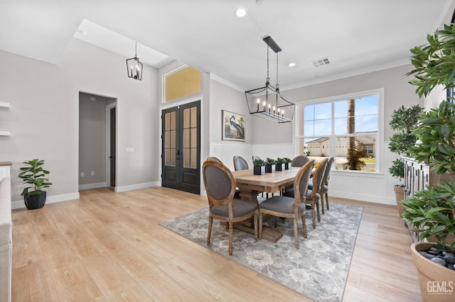 dining space with light hardwood / wood-style floors, an inviting chandelier, ornamental molding, and french doors