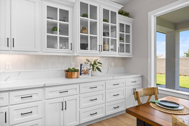 bar featuring white cabinets, decorative backsplash, light hardwood / wood-style flooring, and light stone counters