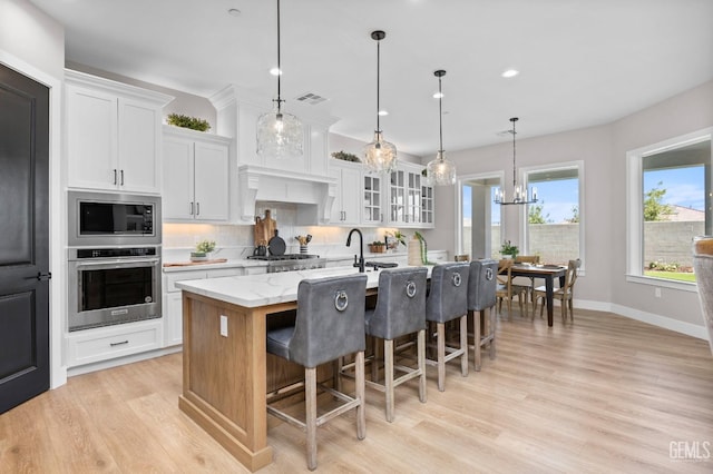 kitchen featuring white cabinetry, decorative light fixtures, a breakfast bar area, a kitchen island with sink, and appliances with stainless steel finishes