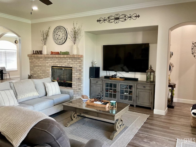 living area featuring crown molding, a fireplace, ceiling fan, wood finished floors, and baseboards