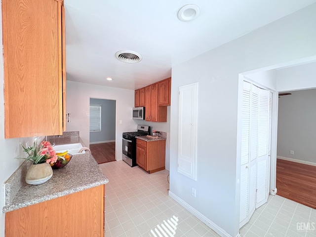 2711 Hubbard St, Bakersfield, CA 93301 - kitchen with appliances with stainless steel finishes, baseboards, light countertops, and brown cabinetry