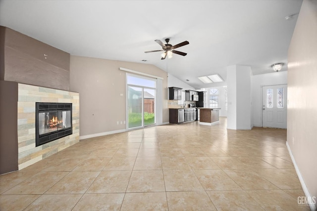 unfurnished living room featuring lofted ceiling, ceiling fan, light tile patterned flooring, a fireplace, and baseboards