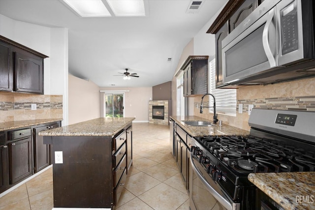 kitchen featuring dark brown cabinetry, visible vents, appliances with stainless steel finishes, a stone fireplace, and a sink