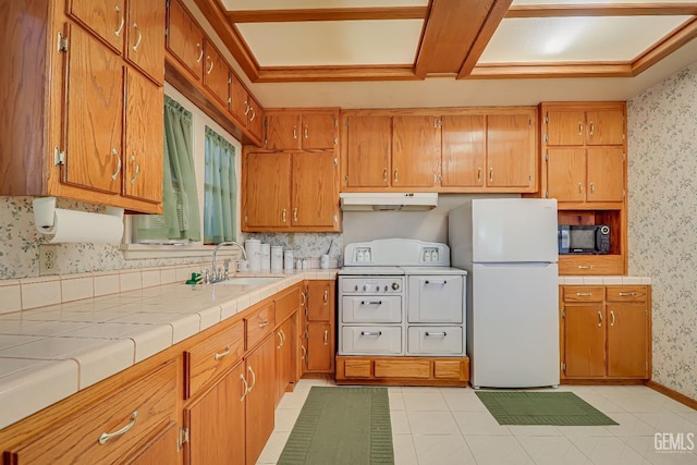 kitchen with wallpapered walls, freestanding refrigerator, a sink, under cabinet range hood, and black microwave