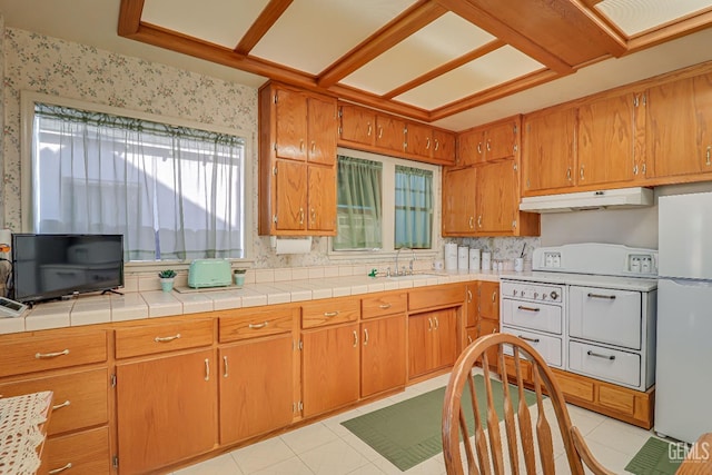 kitchen featuring under cabinet range hood, light tile patterned floors, white appliances, and a sink