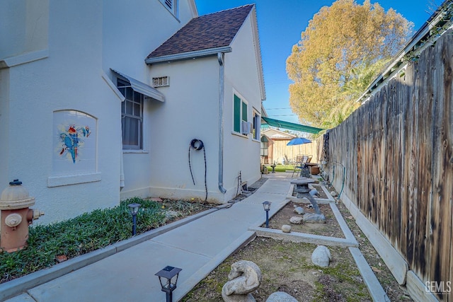 view of property exterior with stucco siding, roof with shingles, and a fenced backyard