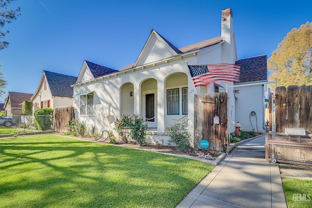 view of front of house with stucco siding, roof with shingles, a front yard, and fence