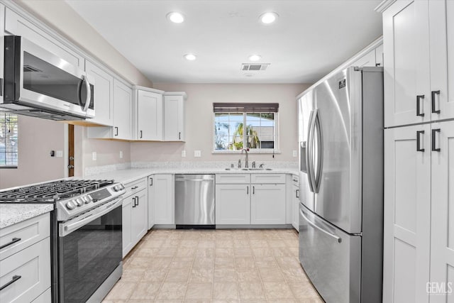 kitchen featuring light stone counters, visible vents, appliances with stainless steel finishes, white cabinetry, and a sink