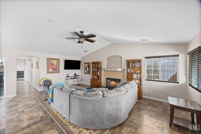 living room with arched walkways, baseboards, vaulted ceiling, stone finish flooring, and a tiled fireplace