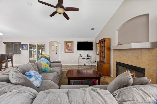 living area with visible vents, a tiled fireplace, a ceiling fan, vaulted ceiling, and baseboards