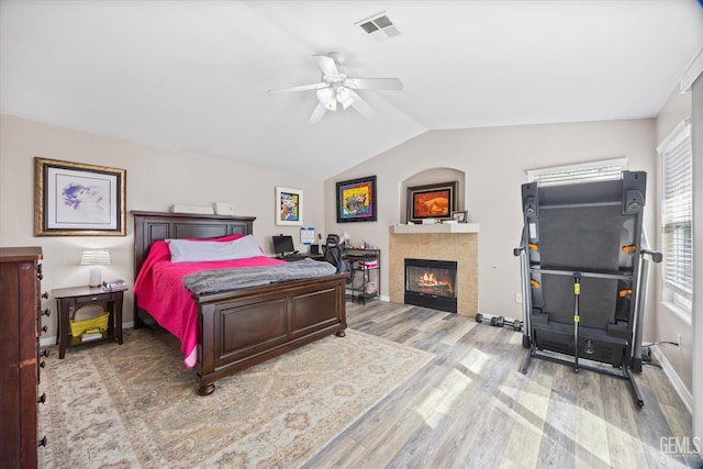 bedroom featuring a fireplace, visible vents, vaulted ceiling, wood finished floors, and baseboards