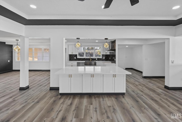 kitchen with white cabinetry, decorative light fixtures, backsplash, a kitchen island, and wall chimney range hood