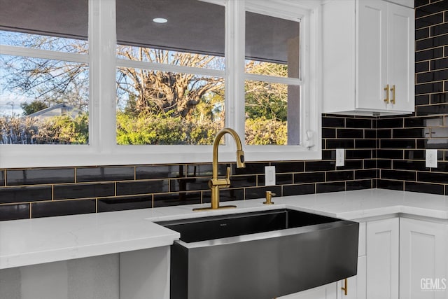 kitchen featuring sink, backsplash, light stone counters, a healthy amount of sunlight, and white cabinets