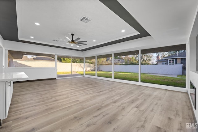 unfurnished sunroom featuring ceiling fan, a raised ceiling, and a wealth of natural light