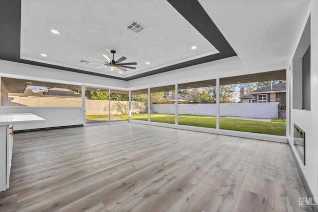 unfurnished sunroom with ceiling fan and a tray ceiling