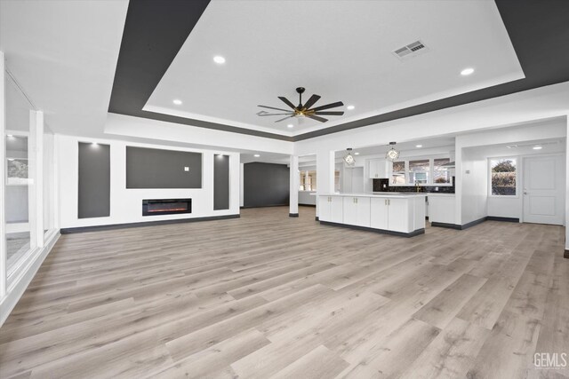 unfurnished living room with ceiling fan, a raised ceiling, and light wood-type flooring