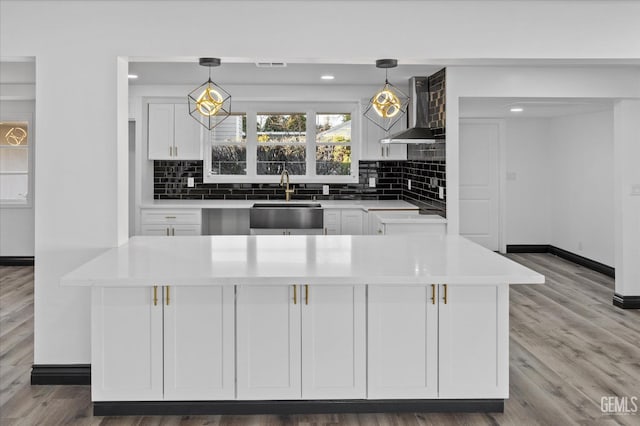 kitchen featuring white cabinetry, wall chimney exhaust hood, sink, and pendant lighting