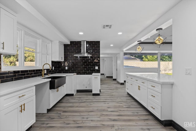 kitchen featuring tasteful backsplash, wall chimney exhaust hood, sink, and white cabinets