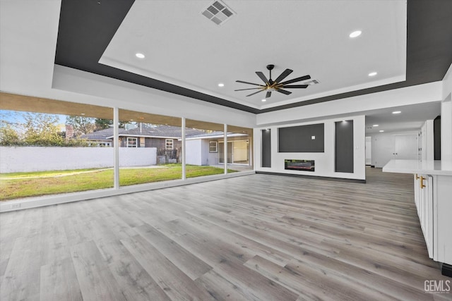 unfurnished living room with light hardwood / wood-style flooring, a raised ceiling, and ceiling fan