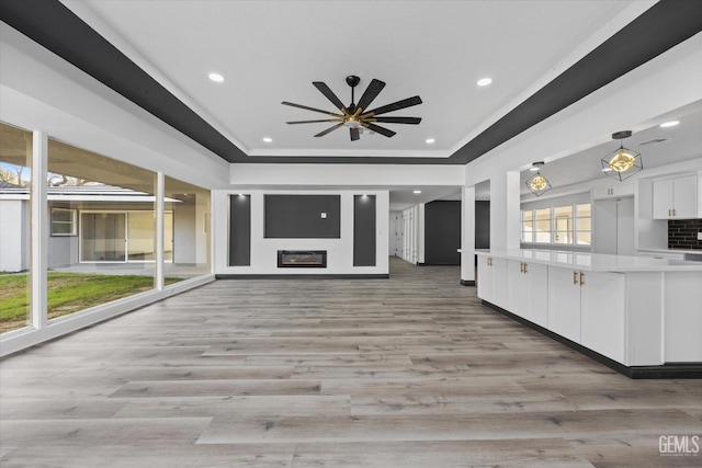 unfurnished living room featuring a tray ceiling, light hardwood / wood-style floors, and ceiling fan