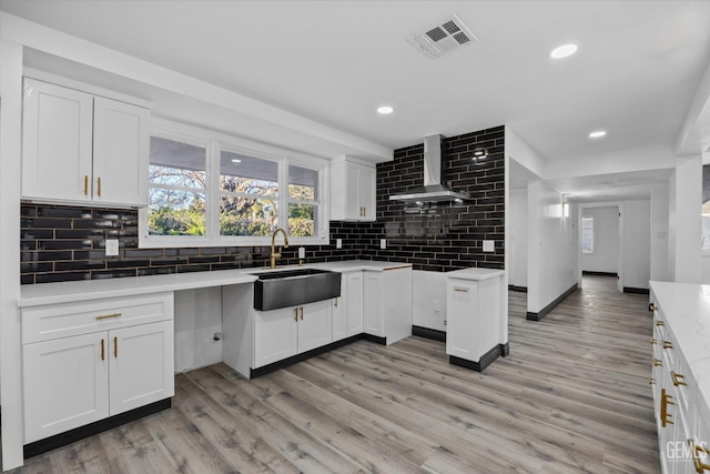 kitchen with white cabinetry, sink, backsplash, light hardwood / wood-style floors, and wall chimney exhaust hood