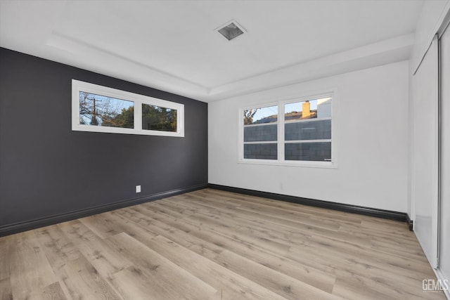 spare room featuring a tray ceiling and light wood-type flooring