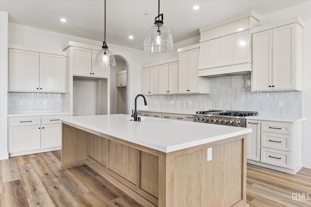 kitchen featuring light wood finished floors, a center island with sink, stainless steel gas cooktop, and white cabinets