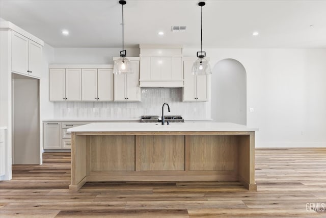 kitchen featuring decorative backsplash, light countertops, arched walkways, and a center island with sink