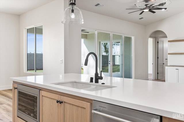 kitchen featuring visible vents, light brown cabinetry, appliances with stainless steel finishes, arched walkways, and a sink