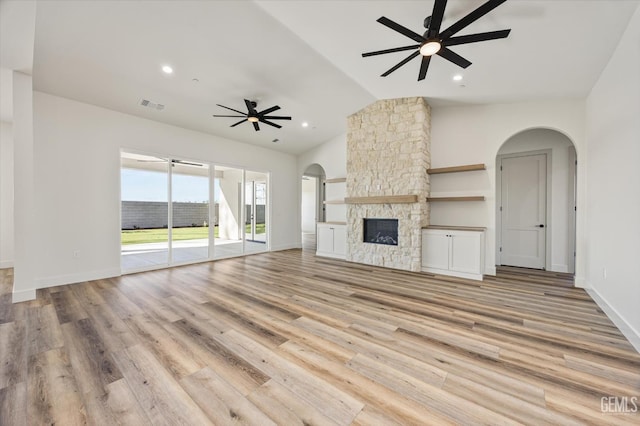 unfurnished living room with a ceiling fan, visible vents, light wood-style flooring, arched walkways, and vaulted ceiling