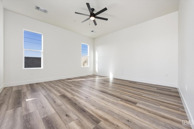 empty room featuring visible vents, baseboards, a ceiling fan, and wood finished floors